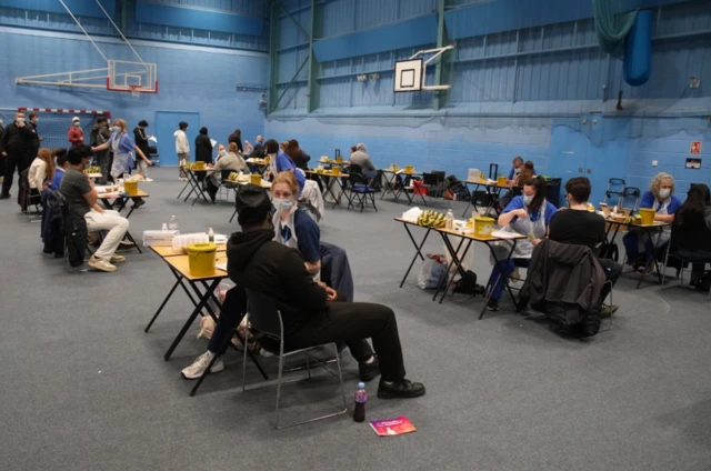 Sports centre at the University of Kent turned into vaccination centre. Tables set up over three rows, each with a medical practitioner speaking to a student receiving a vaccine