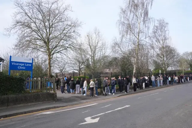 People wait in line outside a meningitis vaccination hub at the Vicarage Lane Clinic in Ashford, Kent.