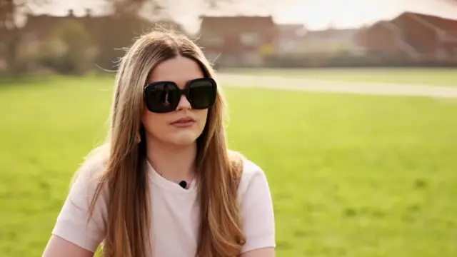 University of Kent student Annabelle Mackay pictured outside wearing sunglasses and a white t-shirt as she speaks to the BBC's Hugh Pym, off camera