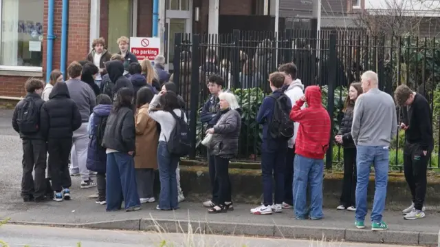 People wait in line outside a meningitis vaccination hub at the Vicarage Lane Clinic in Ashford, Kent.