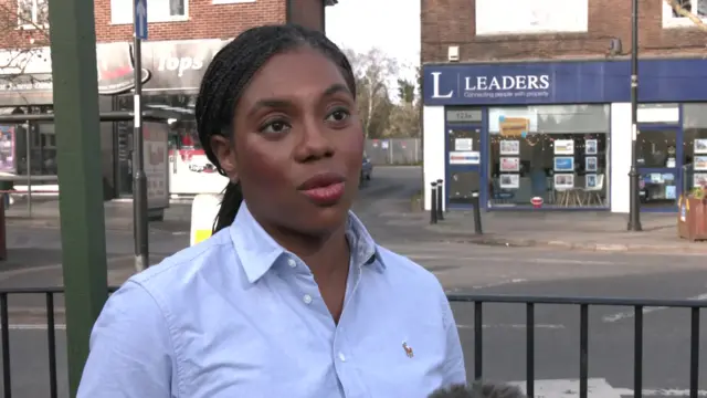 Kemi Badenoch wearing a blue shirt and standing on a high street