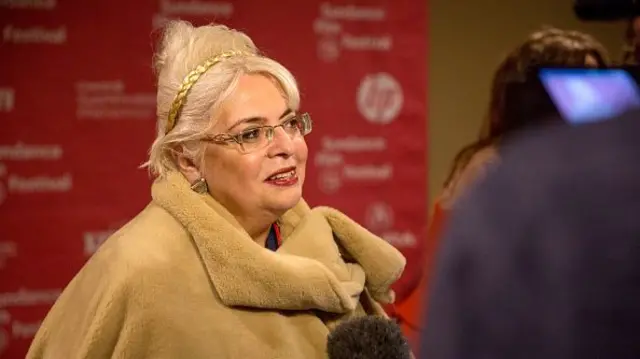 A blonde woman speaks on the red carpet