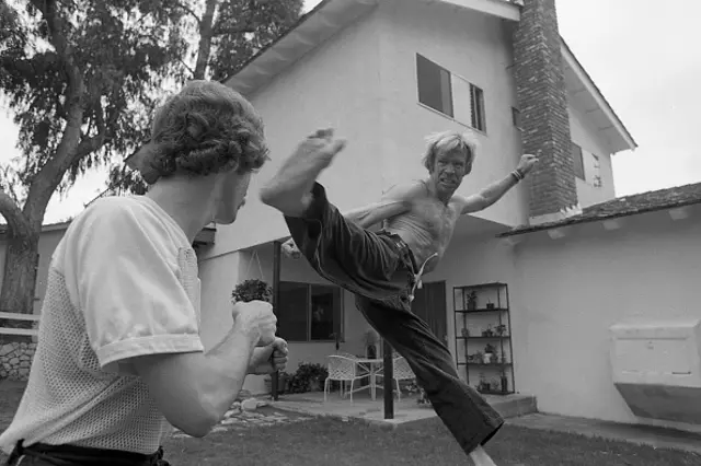 Black and white photograph showing Chuck Norris kicking someone in the face