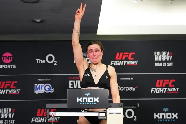 Melissa Mullins holds up her arm and holds back tears as she stands on weighing scales
