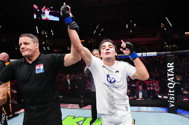 Luke Riley has his arm raised by Marc Goddard and holds up one finger