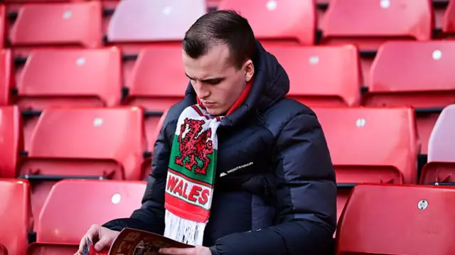 A Wrexham fan with a Wales scarf on reading the match programme at Bramall Lane