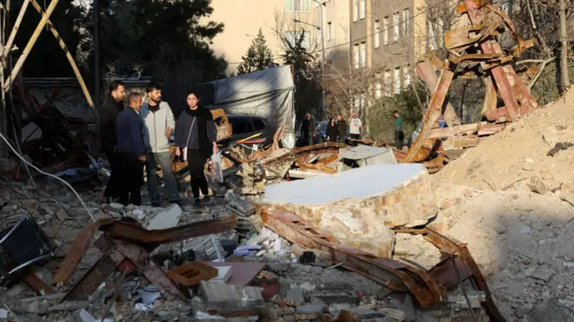 Three men and a woman walk among the rubble of a destroyed building in Tehran