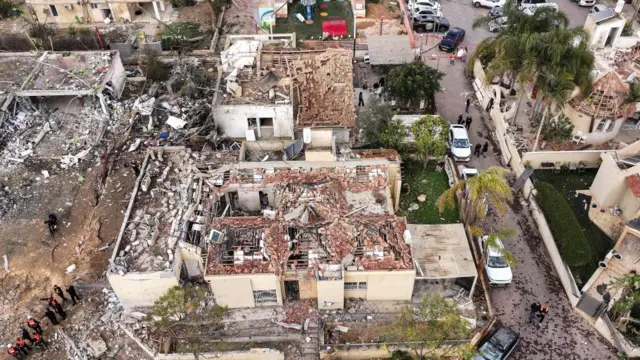 A drone view shows several destroyed buildings. The roof tiles of the buildings have pealed away showing the wooden structures underneath