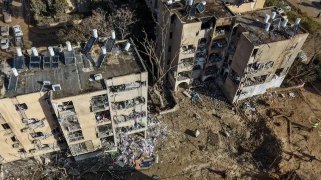 A drone view shows a crater in a residential neighbourhood. An apartment block has also been damaged and debris is spread on the street