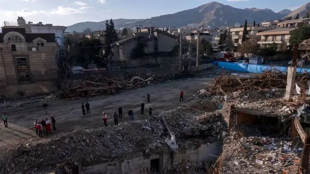 Civilians and emergency workers look upon the remains of a residential and commercial building on March 21, 2026 in the Shahrak-e Gharb neighbourhood of Tehran, Iran.