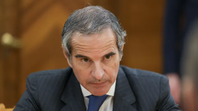 IAEA head Rafael Grossi sitting down. He's in a grey pinstripe suit, white shirt and blue tie, behind him in the blurred background is a wooden door