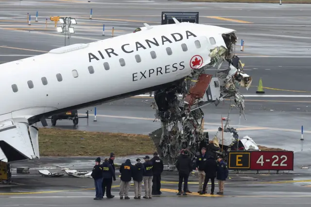 The mangled front of a single aisle Air Canada Express passenger jet looms over a group of crash scene investigators at New York's LaGuardia Airport