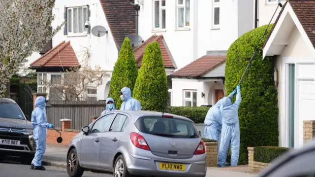Police in forensic suits are searching drain pipes, and guttering