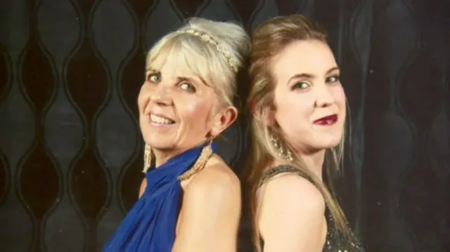 Natalie McNally and her mother, standing back to back. Her mother has blonde hair, tied up and is wearing a blue dress. Natalie has brown hair, tied up and she is wearing a dark coloured dress.