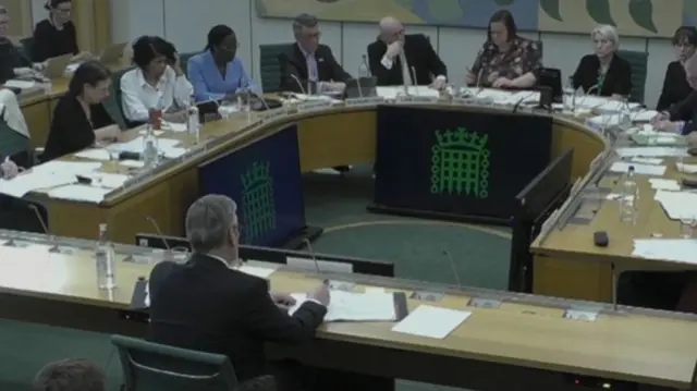 Keir Starmer facing questions from the Liaison Committee. He sits at a wooden table with MPs sat opposite around a horseshoe shaped table.