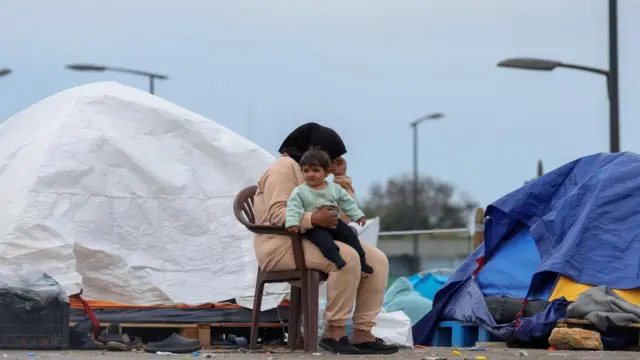 A woman sits as she holds a baby at a temporary encampment for displaced people, in Beirut