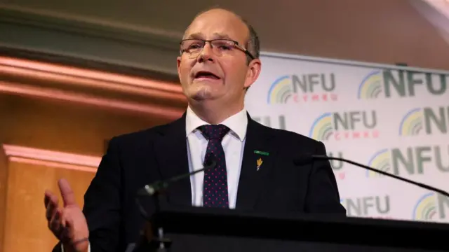 Tom Bradshaw speaking at an event, there is a microphone in front of him