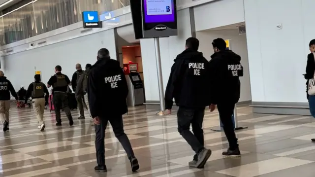 several ICE agents walking through an airport hallway
