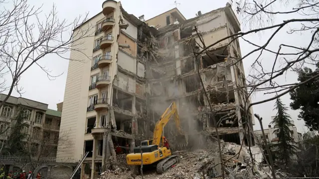 A digger combs through a building which has been torn in half by an airstrike