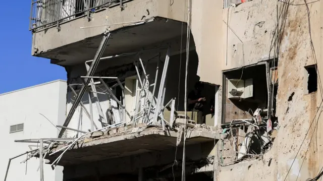 Debris hangs from a damaged building at the site following Iranian missile barrages in central Israel, amid the U.S.-Israel conflict with Iran, in Tel Aviv, Israel, March 24, 2026.