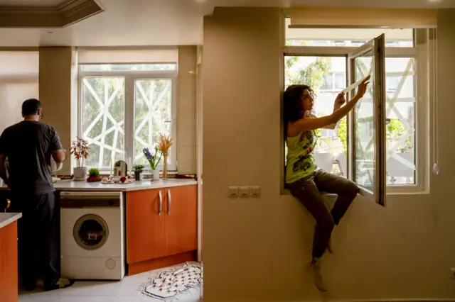 A person tapes a window as another works in the kitchen in a home in Tehran on Tuesday