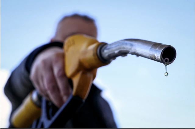 A drop of petrol falls from the nozzle of a petrol pump.