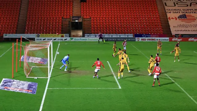 Players from Doncaster and Port Vale stand and watch as the ball flies towards the net