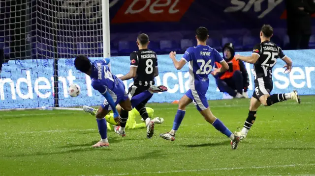 Kane Drummond (left) watches as the ball goes into the net as players from both teams run behind him towards the goal