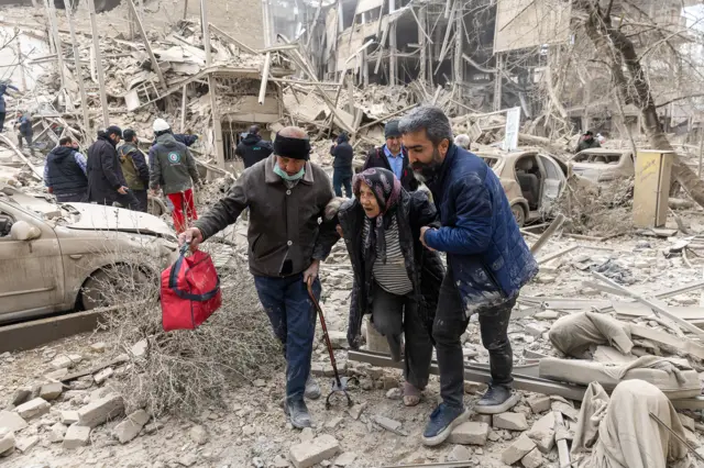 A woman is pulled by two men away from rubble and debris following US-Israeli attacks on Tehran on 16 March