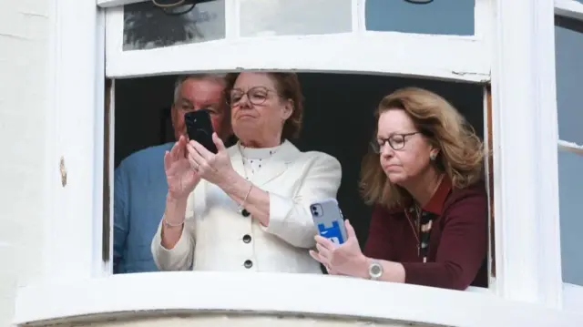 Two women and a man lean out of a window taking photos