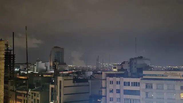 Smoke rises over buildings in an otherwise dark Tehran, Iran