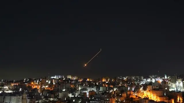 An orange line is drawn across the night sky above the city of Hebron following a missile