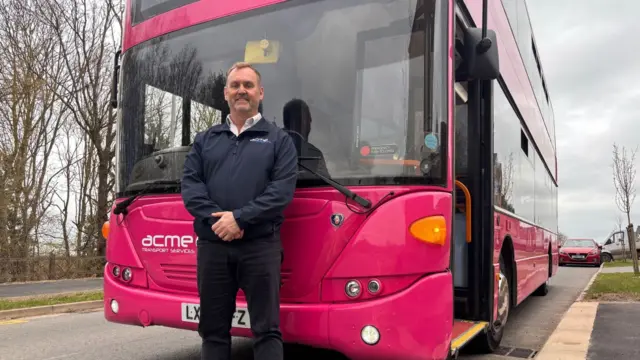 A man stands in front of a pink bus