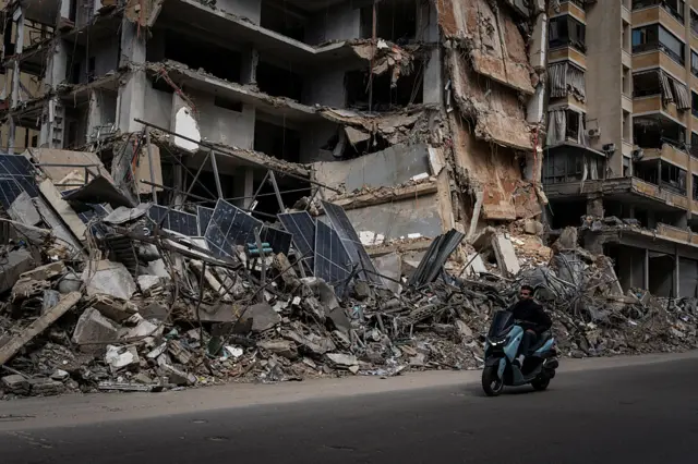 man rides on a motorbike in front of the aftermath of an IDF strike in the area of Dahiye