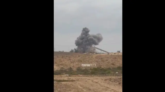 A dark smoke plume erupts from a mine site at the top of a hill.