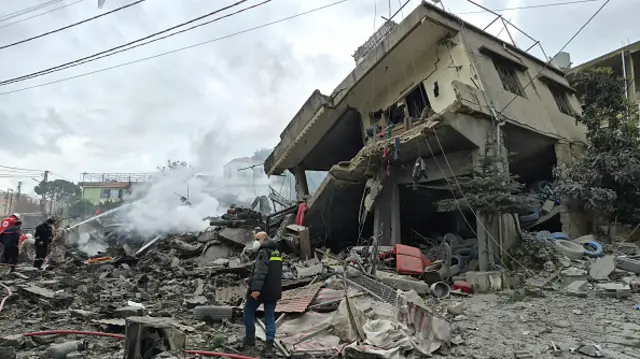 A man looks over his shoulder as he walks through the rubble towards a building that has partially collapsed following a strike