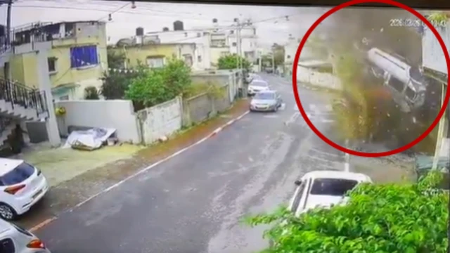 A grab from CCTV shows a street with parked cars and in the right hand corner an upside down car in mid-air with smoke all around it, with a red circle overlain to highlight the scene