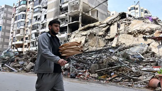 A man walks down the street past a completely leveled building