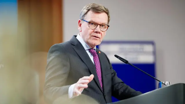 German foreign minister Johann Wadephul in a dark, pinstriped suit and purple tie, speaking at a lectern.