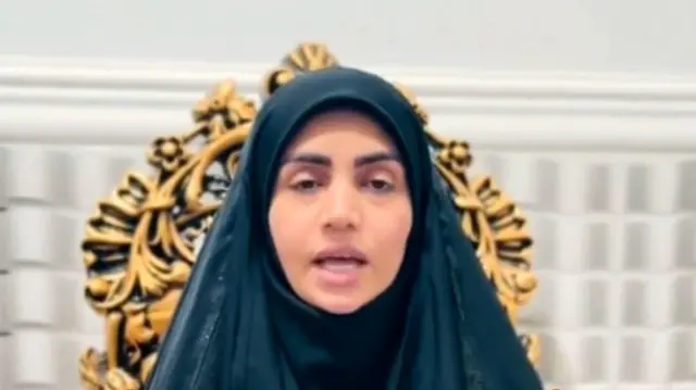 A woman in an Islamic religious head covering speaks on a gold-and-black backed chair.