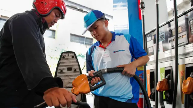 A worker refuels a motorcycle at a petrol station in Bangkok, Thailand
