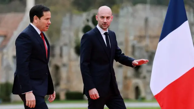 Marco Rubio walks alongside  French foreign minister Jean-Noel Barrot in a French village with a French flag in frame.