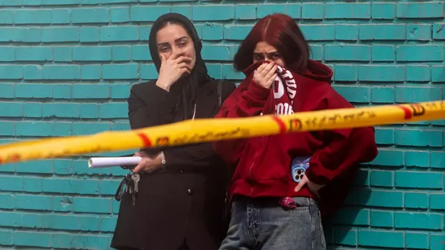 two young women covering their faces and looking distressed in front of caution tape