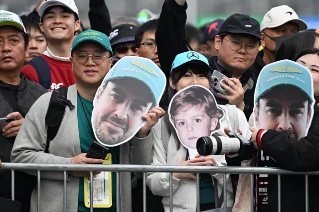 Fans hold up Fernando Alonso heads in the fanzone