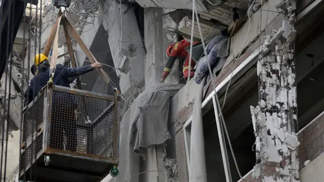 rescue workers in a lift next to a damaged building