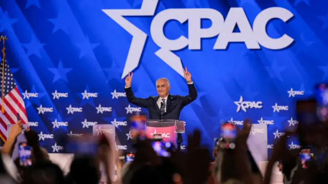 Pahlavi holds fingers in a peace sign in front of a crowd