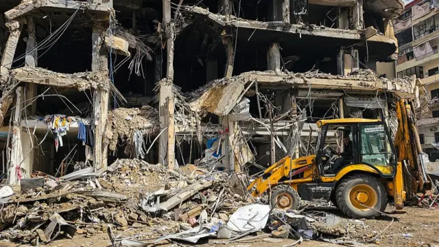 A bulldozer in front of a largely destroyed building