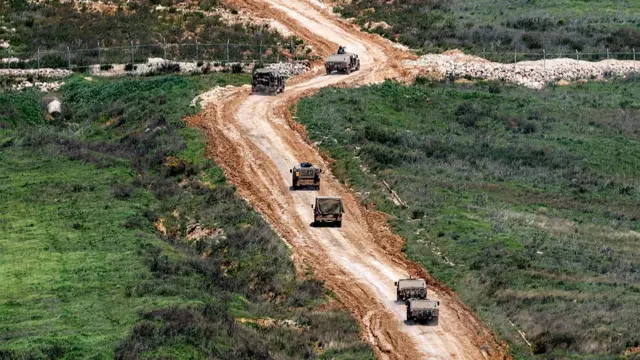 A line of tanks driving up a dirt road surrounded by green grass.