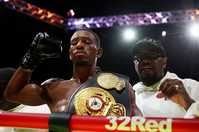 Ezra Taylor holds up his fist next to some boxing ring ropes
