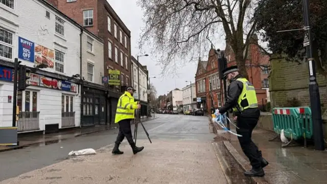 Police officers removing tape from across the road